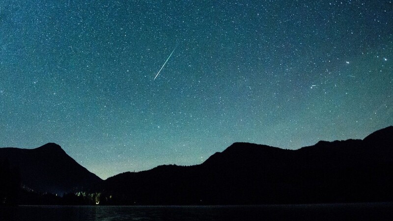 Eine Sternschnuppe leuchtet neben der Milchstraße am Himmel über dem Walchensee.