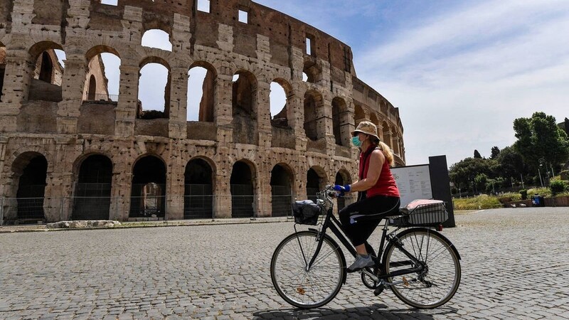 Eine Radlerin mit Mundschutz vor dem Kolosseum.