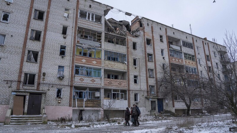 Anwohner gehen vor einem durch Beschuss zerstörten Haus in der Ukraine spazieren.
