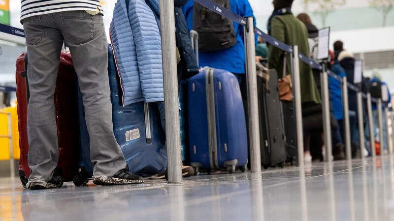 Passagiere stehen mit ihrem Gepäck an Check-in-Schaltern am Flughafen München.