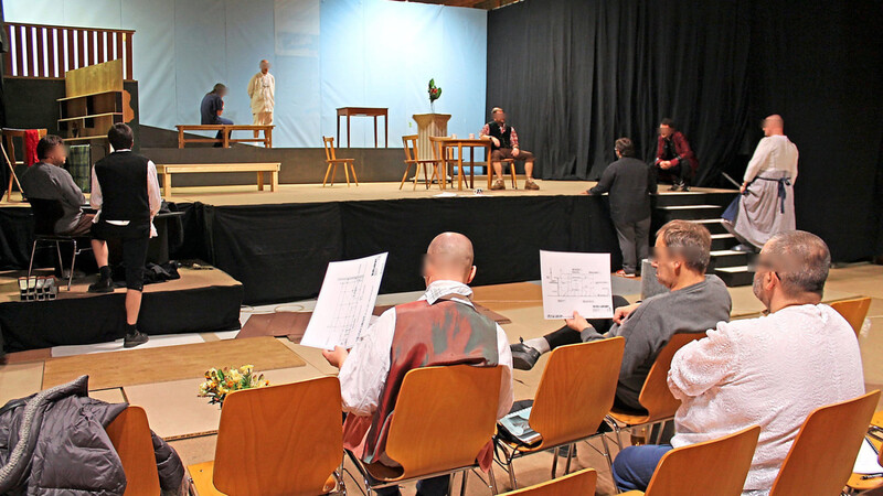 Theater-Probe in der Mehrzweckhalle der JVA: Auf der Bühne wird am Feinschliff einer Szene gefeilt, von den Schauspielern im Publikum die Bühnenskizzen gewälzt.