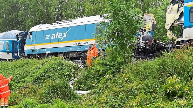 Einsatzkräfte stehen am Unfallort, an dem am Vortag ein Schnellzug aus München mit einem entgegenkommenden Regionalzug zusammengestoßen ist. Mit schwerem Gerät begannen am Donnerstag die Aufräumarbeiten