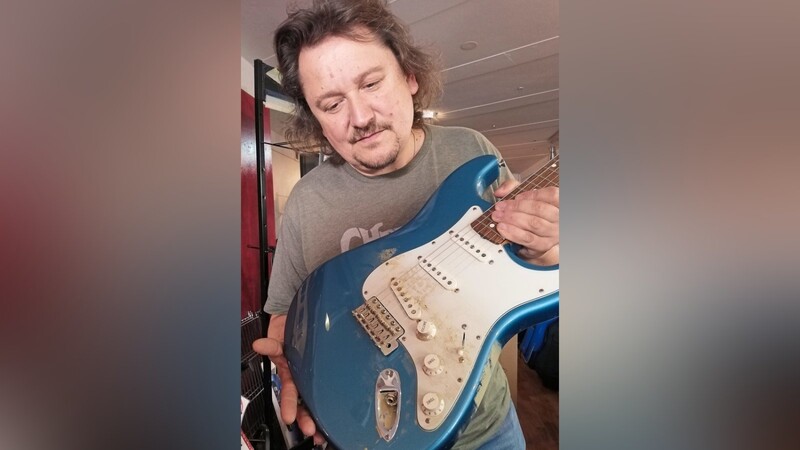 Mick Krämer mit einer sandigen Gitarre, die bei ihm gerade in der Werkstatt zur Reparatur ist.