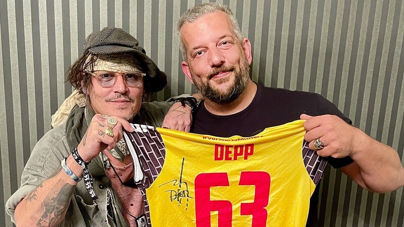 Johnny Depp (l.) und der in Suhl lebende Musiker Alexander Becker halten zusammen ein Trikot des Volleyball-Bundesligisten VfB Suhl.