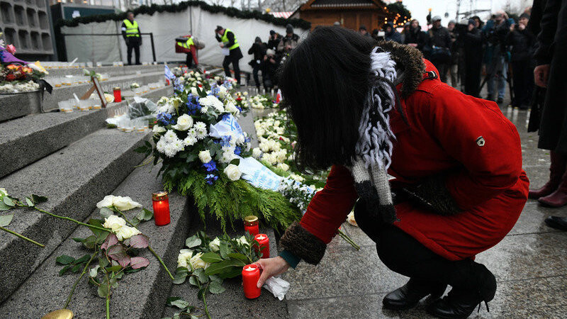 Passanten stellen am 19.12.2017 an der Gedenkstätte auf dem Weihnachtsmarkt an der Gedächtniskirche in Berlin Blumen und Kerzen ab.