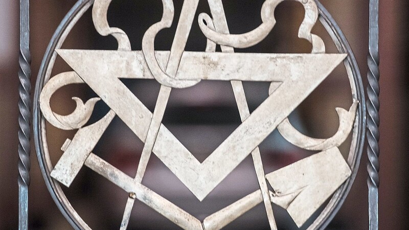 Zirkel, Dreieck, Hammer und Maurerkelle an einem Tor zu einer Freimaurerloge: Symbole wie diese sind eng mit der Freimaurerei verbunden.