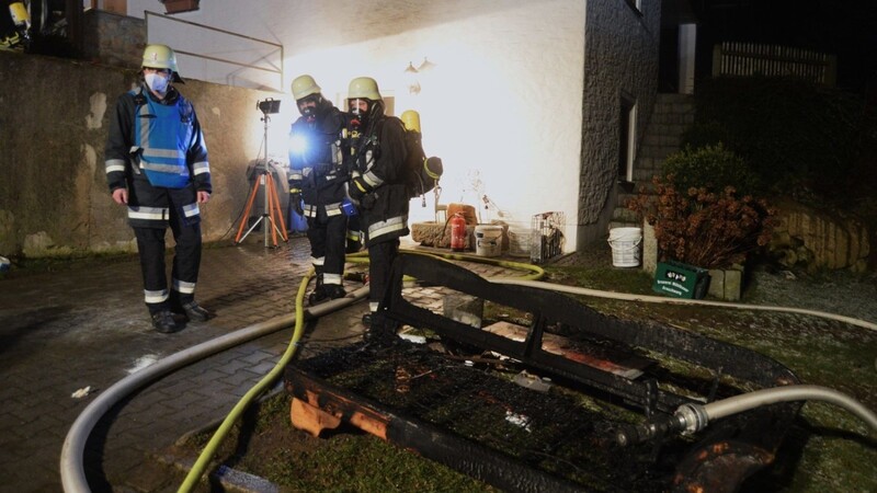 Feuerwehrleute unter Atemschutz holen eine brennende Couch aus einem verrauchten Kellerraum.