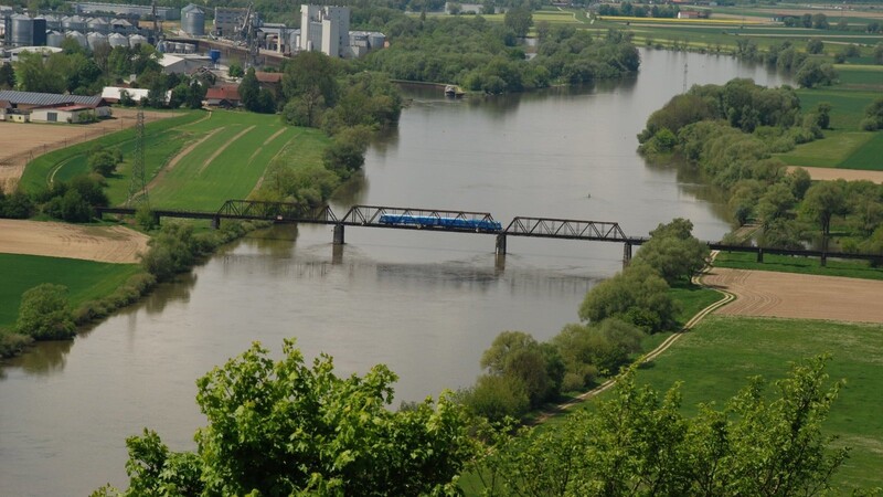 Eine blaue Garnitur der Gäubodenbahn rollt über die alte Eisenbahnbrücke. Derzeit wird an einem Neubau der Donauüberquerung geplant.
