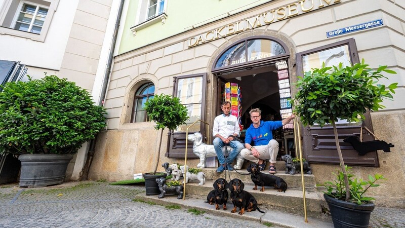 Seppi Küblbeck (l) und Oliver Storz sitzen mit ihren Dackeln vor ihrem Dackelmuseum.