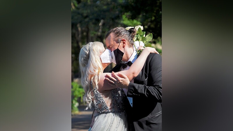 Ein Paar küsst sich mit aufgesetzten Masken in einem Park. So sahen im vergangenen Jahr viele Hochzeiten aus. Das Bangen um die Feiern geht jedoch weiter.