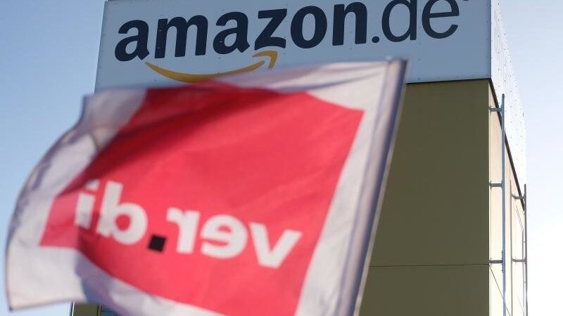 Eine Fahne der Gewerkschaft Verdi weht an einem Zaun des Leipziger Logistikzentrums von Amazon.