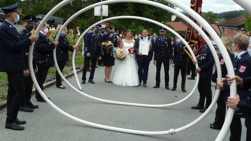 Die Führungsspitze der FFWTraitsching gratuliert Carola und Thomas Wittmann nach der Hochzeitsmesse unter einer Schlauchspirale.