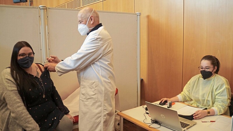 Symbolisch demonstriert Heinz Huf, Allgemeinmediziner im Ruhestand, an Tamara Bohlein, wie die Impfung durchzuführen ist. Rechts im Bild sitzt Melissa Schnaidt. Alle drei sind für den BRK-Kreisverband tätig.