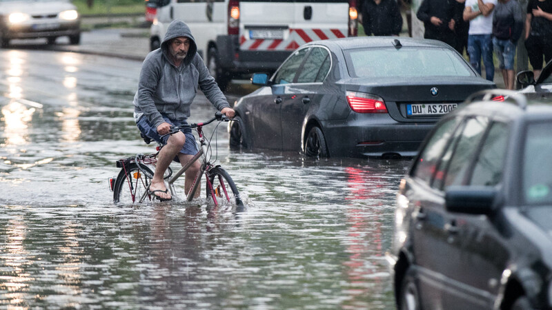 Ein Radfahrer fährt über eine überflutete Straße an liegen gebliebenen Autos vorbei.