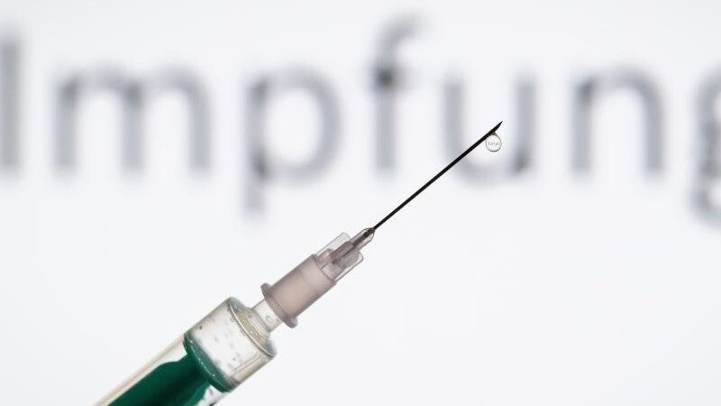 Eine Spritze wird vor den Schriftzug "Impfung" gehalten.