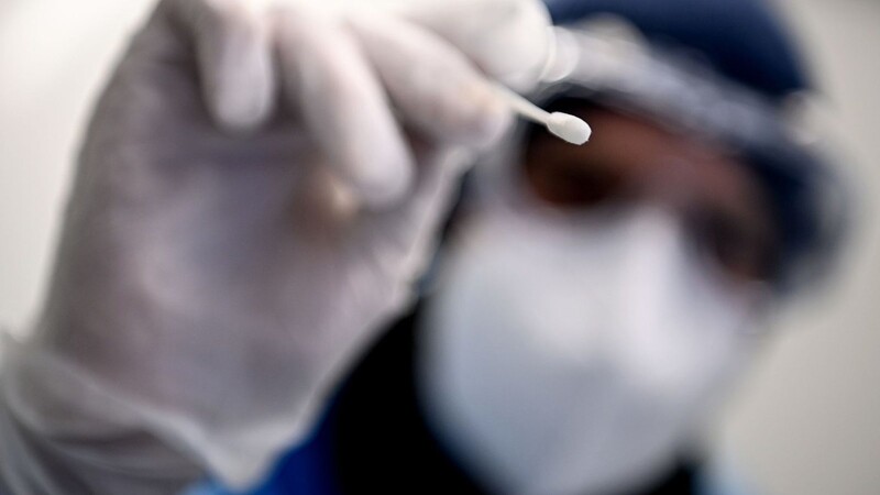 Ein Arzt hält ein Teststäbchen für die Entnahme einer Probe für einen Corona-Test in der Hand.
