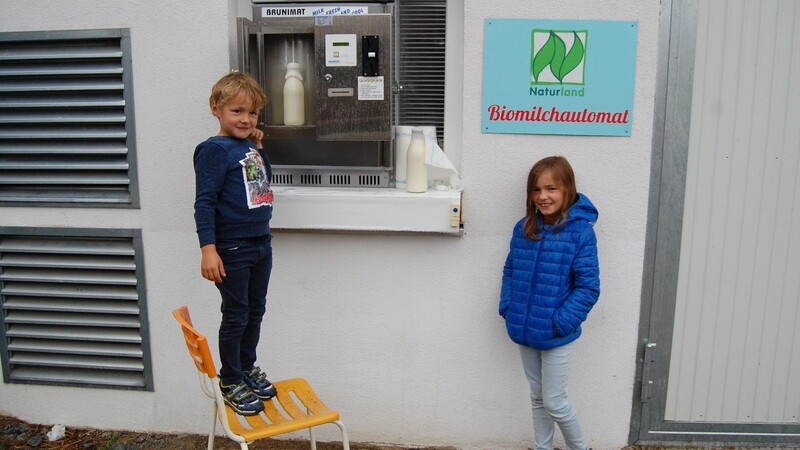 Louis und Lea Koller zeigen, wo an der Biomilchtankstelle am Kollerhof frische Milch gezapft werden kann.