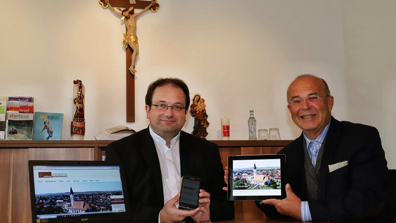 Pfarrer Jürgen Josef Eckl und Gerulf Belhane (r.) präsentieren die neue digitale Aufstellung der Pfarrei.