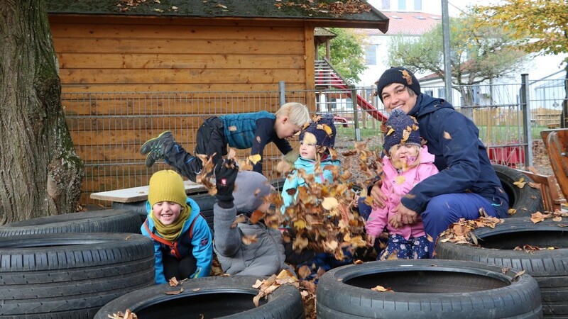 Erzieherin Kathrin Zeilhofer spielt mit einigen Kindern der Naturgruppe im selbst gebauten Blätterbad mit einer Umrandung aus Altreifen.