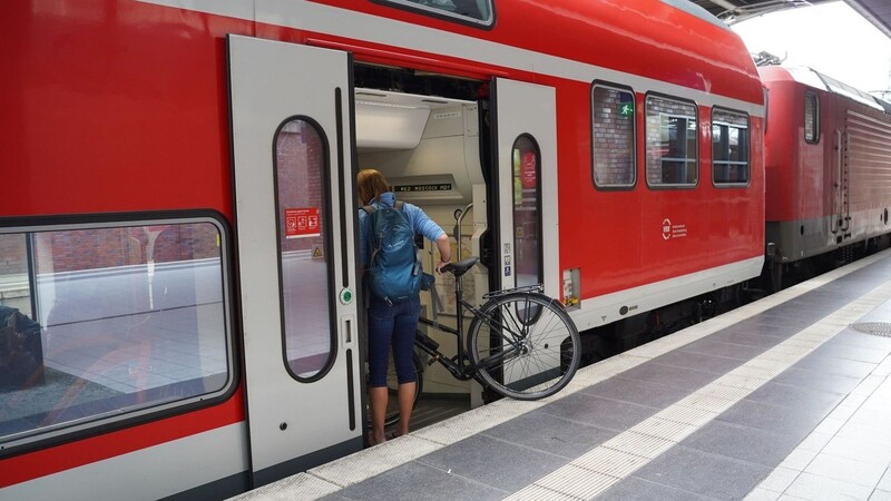 Eine Reisende steigt mit ihrem Fahrrad in eine Regionalbahn Richtung Rostock.