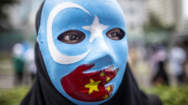 Ein Teilnehmer einer Demonstration vor der chinesischen Botschaft trägt eine Maske mit den Farben der Flagge der uigurischen Unabhängigkeitsbewegung und einer aufgemalten roten Hand mit den Sternen der chinesischen Nationalflagge.