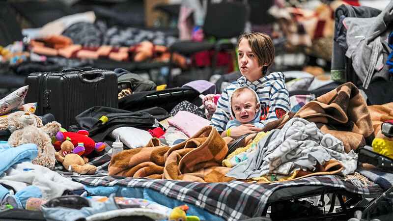 Gestrandet, aber in Sicherheit: Ein Kind sitzt mit einem Baby im Arm in einem Haufen von Decken in einem Flüchtlingszentrum im polnischen Nadarzyn.