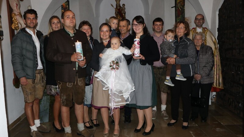 Die Taufpatin Simone Baumann, die den Täufling in den Armen hält, und die Eltern werden von der Taufgemeinschaft und Kaplan Florian Rein umrahmt.