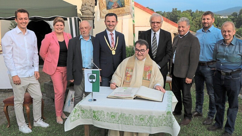Pfarrer Herbert Mader trägt sich ins Ehrenbuch der Stadt in Anwesenheit von Bürgermeister Markus Hofmann und mehrerer Stadträte ein.