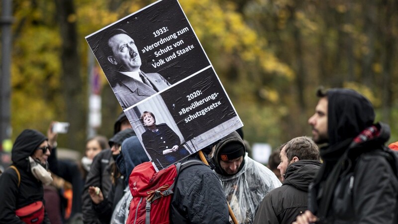 Ein Demonstrant unterstellt Gemeinsamkeiten in der Politik von Adolf Hitler und Angela Merkel.