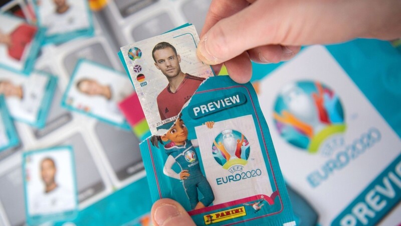 Ein Mitarbeiter des Panini-Verlags öffnet über einem Panini-Preview-Sammelalbum zur Fußball-Europameisterschaft 2020 ein Sticker-Tütchen.