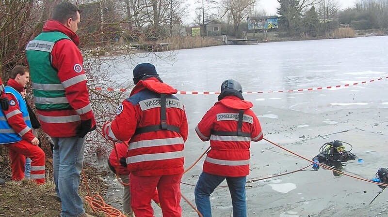 Notweniges Training, um für den Ernstfall bestmöglich vorbereitet zu sein: Zwei Eistaucher der Wasserwacht üben die Rettung von im Eis eingebrochenen Personen. Mehrere Kollegen sichern sie dabei mit Seilen.