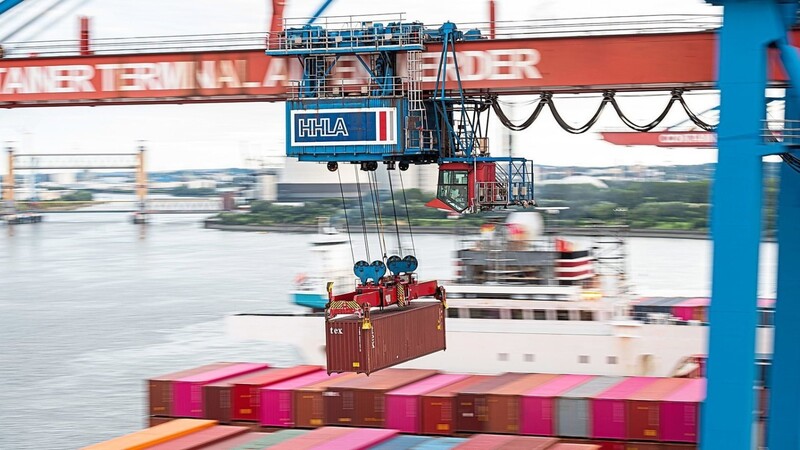 Ein Container wird auf einem Terminal im Hamburger Hafen mit einer Containerbrücke auf ein Schiff geladen. Seit Mai steigen die Exportzahlen an. Doch die Corona-Rezession macht sich immer noch bemerkbar.