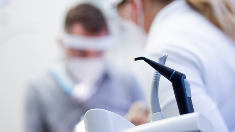 Ein Zahnarzt und eine Zahnarzthelferin mit Mund-Nasen-Schutz und Schutzvisieren versorgen eine Patientin in einer Praxis. Die Bundeszahnärztekammer weißt darauf hin, die Corona-Pandemie nicht zum Anlass zu nehmen, notwendige Behandlungen und Vorsorgeuntersuchungen beim Zahnarzt zu verschieben.