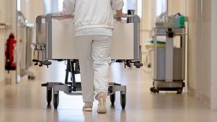 Eine Krankenpflegerin schiebt ein Krankenbett durch einen Flur.