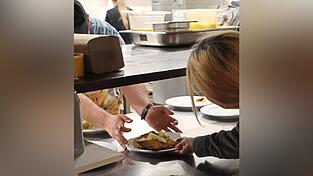 Die Gesch&auml;ftsleiterin holt das frisch gebackene Schnitzel mit Kartoffelsalat aus der K&uuml;che - gleich wird es auf dem Tisch einer Besucherin serviert.