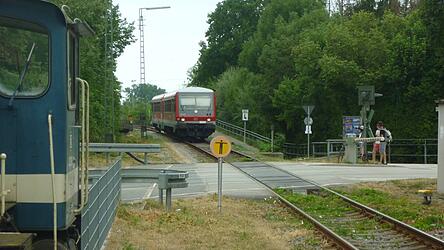 Die G&auml;ubodenbahn bei ihrer Einfahrt in Bogen, aufgenommen im Sommer 2025: Gerade hat sie die Br&uuml;cke &uuml;ber die Staatsstra&szlig;e befahren - erkennbar am Gel&auml;nder links hinter dem Zug -, sogleich wird sie die Schrankenanlage der Bahnhofstra&szlig;e (Kreisstra&szlig;e SR 3) passieren und dann an ihrer Endstation im Bahnhof Bogen halten. Auch die Staatsstra&szlig;enbr&uuml;cke muss neu errichtet werden, wenn es zum Ersatzbau f&uuml;r die Donaubr&uuml;cke kommt.