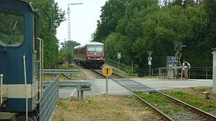 Die G&auml;ubodenbahn bei ihrer Einfahrt in Bogen, aufgenommen im Sommer 2025: Gerade hat sie die Br&uuml;cke &uuml;ber die Staatsstra&szlig;e befahren - erkennbar am Gel&auml;nder links hinter dem Zug -, sogleich wird sie die Schrankenanlage der Bahnhofstra&szlig;e (Kreisstra&szlig;e SR 3) passieren und dann an ihrer Endstation im Bahnhof Bogen halten. Auch die Staatsstra&szlig;enbr&uuml;cke muss neu errichtet werden, wenn es zum Ersatzbau f&uuml;r die Donaubr&uuml;cke kommt.