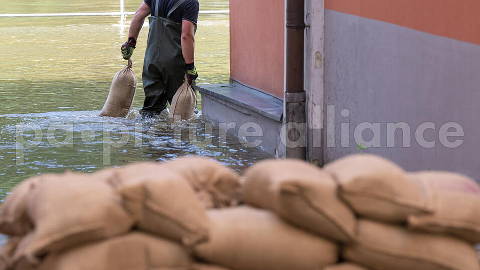 Ein Mann trägt Sandsäcke um Abdichten von Türen und Fenstern durch das Wasser der Donau, das auf der Uferpromenade der Stadt Passau steht. Ein Mann trägt Sandsäcke um Abdichten von Türen und Fenstern durch das Wasser der Donau, das auf der Uferpromenade der Stadt Passau steht.