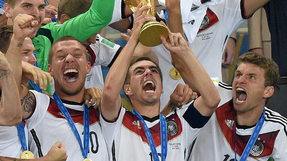 Philipp Lahm (mitte) jubelt mit dem WM-Pokal zwischen seinen Teamkollegen Lukas Podolski (links) und Thomas M&uuml;ller (rechts) w&auml;hrend der Siegerehrung auf der Trib&uuml;ne nach dem Sieg im Fu&szlig;ball-WM-Finale 2014.