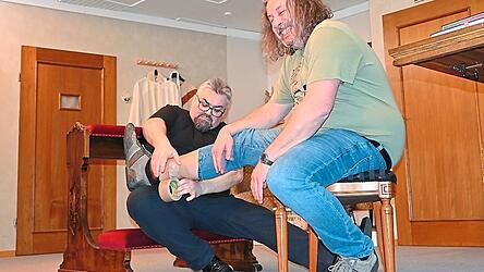 Der Pfarrer befestigt beim aufgezwungenen Gefangenen die Fu&szlig;fessel.