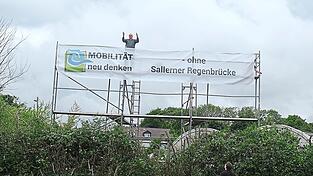 An einem Gerüst auf dem Geländer der vom Brückenbau betroffenen Gärtnerei Hauner hängt seit Samstag ein neun Meter langes Banner des Bündnisses „Mobilität neu denken“.