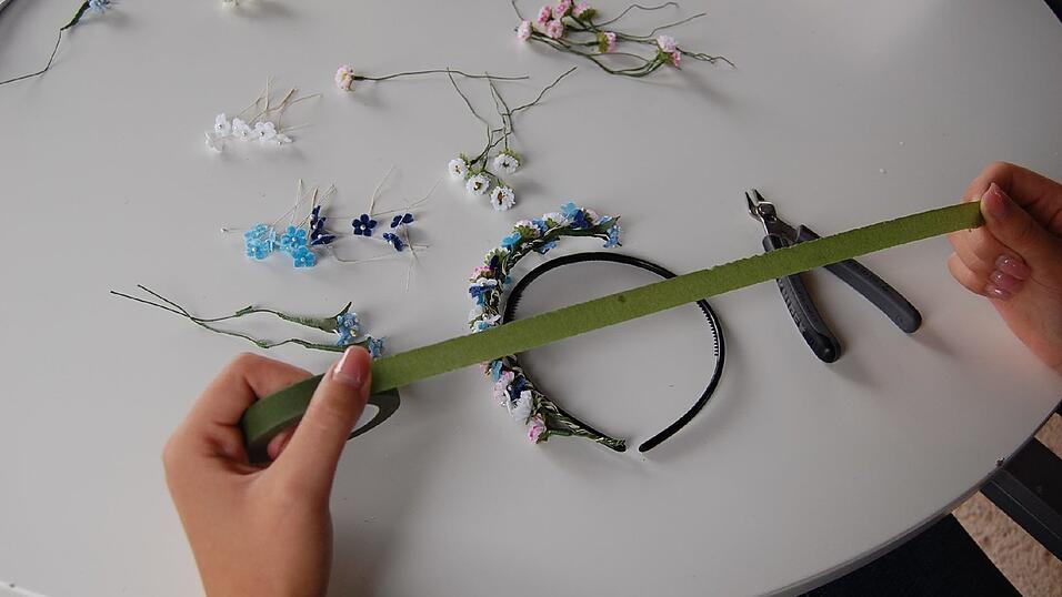 4. Dann etwa 30 Zentimeter Klebeband abreißen. Das Blumengebinde auf den Haarreif legen und an dem Drahtstück, auf dem keine Blüten sitzen, beginnen, Reif und Draht mit dem Klebeband zu umwickeln. Nicht zu straff ziehen, das Klebeband reißt leicht. 4. Dann etwa 30 Zentimeter Klebeband abreißen. Das Blumengebinde auf den Haarreif legen und an dem Drahtstück, auf dem keine Blüten sitzen, beginnen, Reif und Draht mit dem Klebeband zu umwickeln. Nicht zu straff ziehen, das Klebeband reißt leicht.