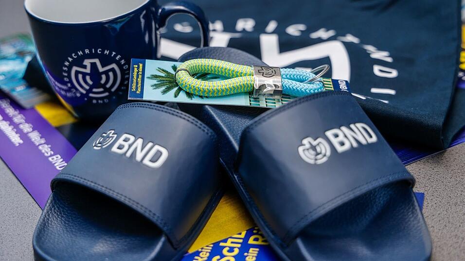 Im Merchandise-Shop gibt es T-Shirts und auch Badelatschen mit BND-Logo. Im Merchandise-Shop gibt es T-Shirts und auch Badelatschen mit BND-Logo.