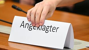 Ein Schild mit der Aufschrift 'Angeklagter' wird auf die Gerichtsbank gestellt.