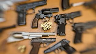 Pistolen und Revolver und Munition liegen auf einem Tisch in einer gesicherten Asservatenkammer.