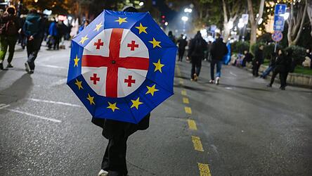Eine Frau mit der europäischen und der georgischen Flagge auf einem Regenschirm bei einer Demo Ende 2024. Die Regierung soll massiv gegen Proteste und unabhängige Medien vorgehen. Wegen eines Stipendiums steht nun auch die Uni Regensburg im Fokus.