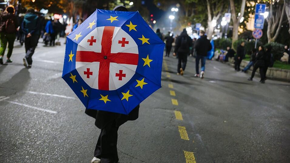 Eine Frau mit der europäischen und der georgischen Flagge auf einem Regenschirm bei einer Demo Ende 2024. Die Regierung soll massiv gegen Proteste und unabhängige Medien vorgehen. Wegen eines Stipendiums steht nun auch die Uni Regensburg im Fokus. Eine Frau mit der europäischen und der georgischen Flagge auf einem Regenschirm bei einer Demo Ende 2024. Die Regierung soll massiv gegen Proteste und unabhängige Medien vorgehen. Wegen eines Stipendiums steht nun auch die Uni Regensburg im Fokus.