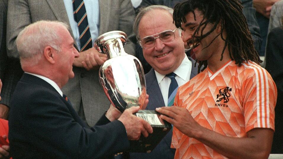M&uuml;nchen, 25. Juni 1988 | Der niederl&auml;ndische St&uuml;rmer Ruud Gullit (r.) empf&auml;ngt den Europameisterpokal aus den H&auml;nden des franz&ouml;sischen UEFA-Pr&auml;sidenten Jacques Georges (l.), Bundeskanzler Helmut Kohl (M.) schaut l&auml;chelnd zu. Die Niederl&auml;nder besiegen im Olympiastadion die Elf der UdSSR mit 2:0.