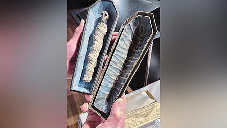 Ein Tischsarg mit einer Puppe, gestaltet wie eine halb verweste Leiche.