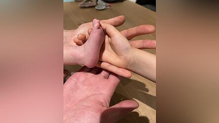 Z&auml;rtlich ber&uuml;hren die Eltern und ihre &auml;lteste Tochter den kleinen Fu&szlig; des Babys, das gesund zur Welt kommen durfte und nun viele Fu&szlig;abdr&uuml;cke in ihrem gemeinsamen Familienleben hinterlassen soll.